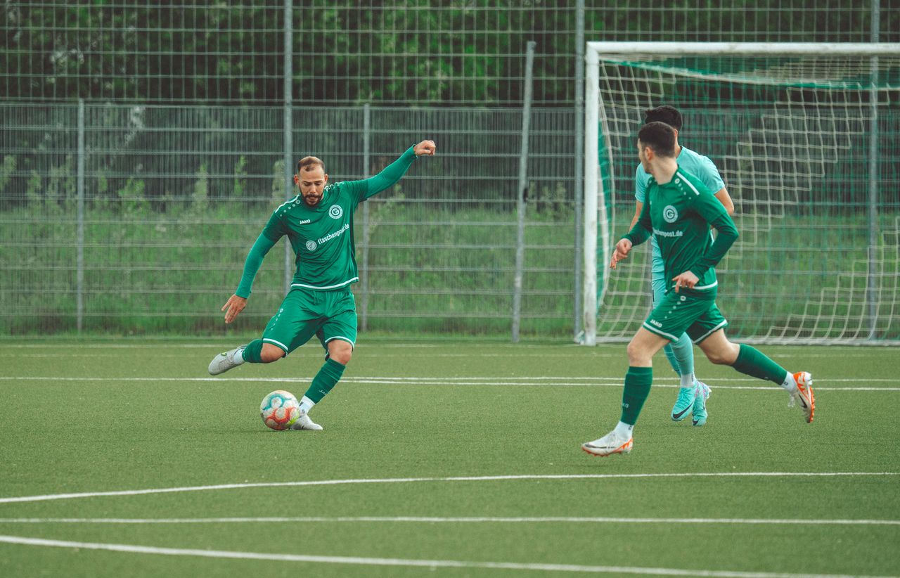why-choose-us-02 Players in green uniforms engage in a dynamic soccer match on a grassy field.