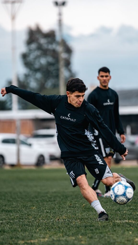 Dynamic shot of a soccer player kicking the ball during practice on a green field.