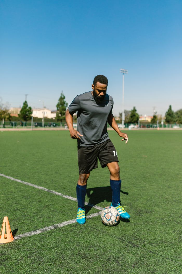 services-05 Athletic man practicing soccer skills on a sunny day outdoors on a green sports field.